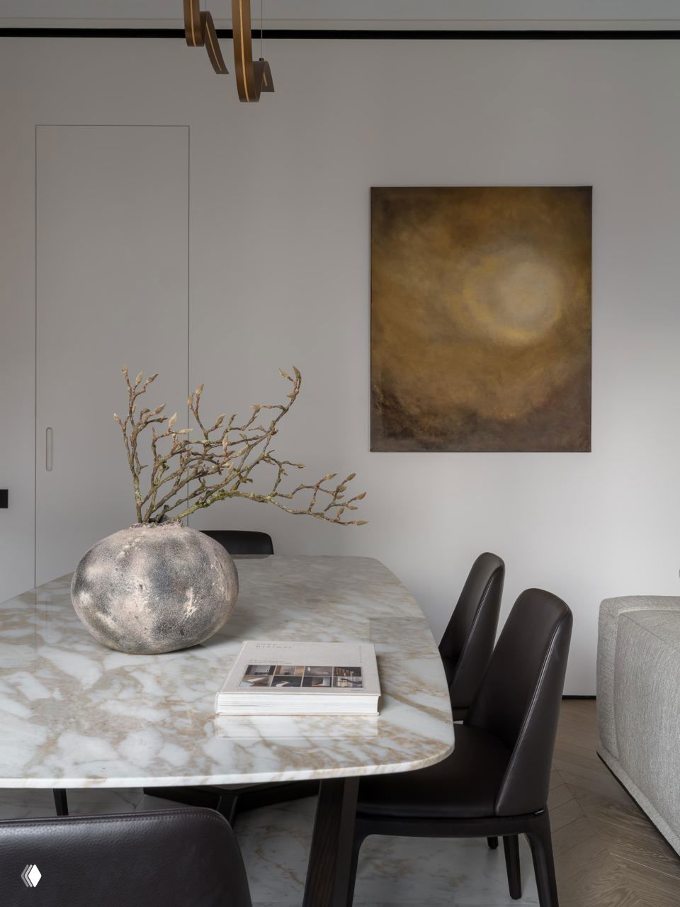 Стол из белого мрамора с декоративной вазой и книгой, на стене абстрактная картина; композиция подчёркивает спокойную бежево-серую палитру интерьера.
