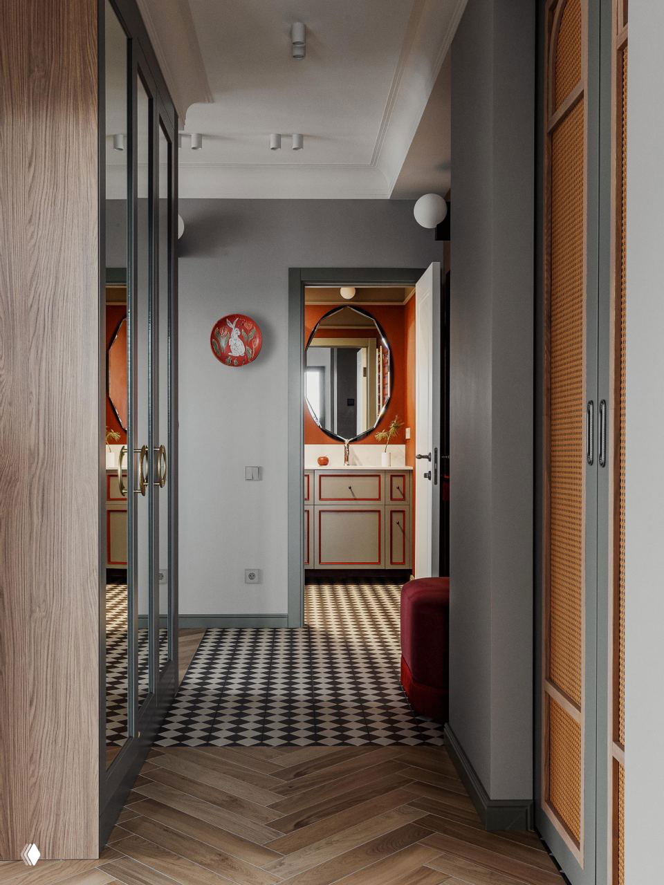 Коридор с чёрно‑белой шахматной плиткой на полу, зеркальные двери шкафа и дверной проём в ванную комнату с оранжевыми акцентами и круглым зеркалом; видна часть паркетного пола.