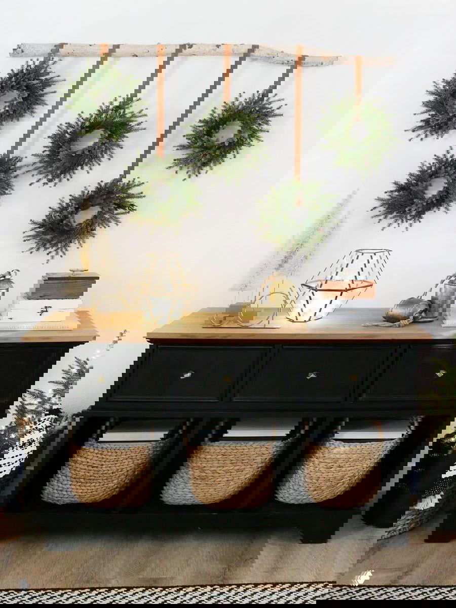 Набор маленьких венков, подвешенных на берёзовой ветке над комодом — идея для создания композиции из повторяющихся элементов на стене.