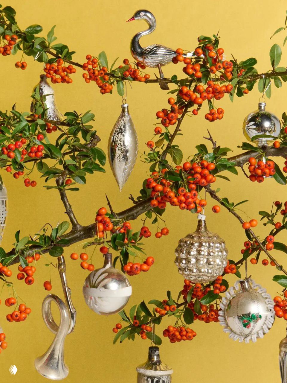 Ветка с ярко‑оранжевыми ягодами, украшенная несколькими винтажными стеклянными шарами и фигурными игрушками разных форм.