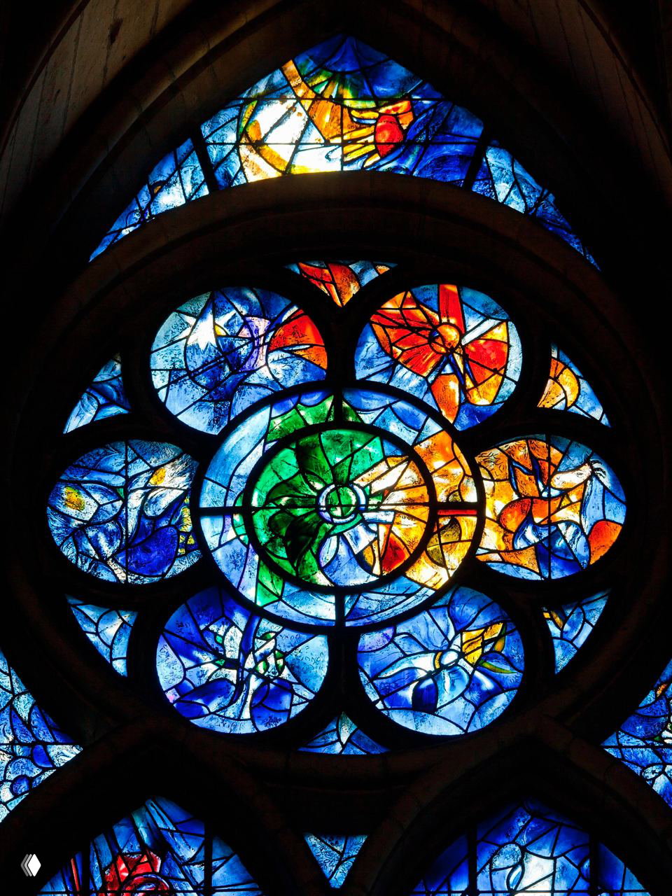 Крупный план цветного витражного окна с геометрическими и растительными мотивами, с насыщенными синими и зелёными тонами.