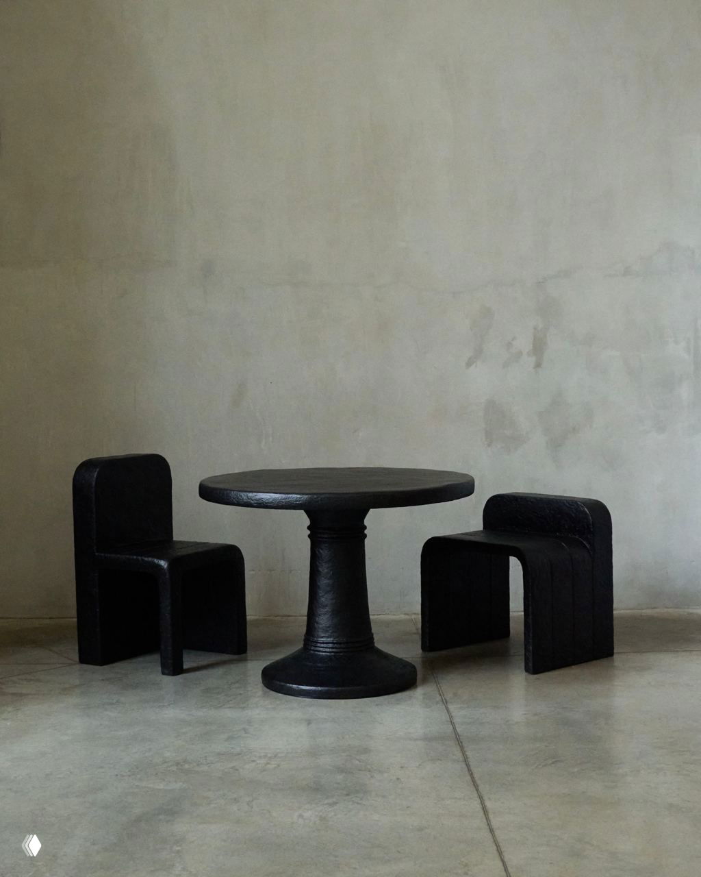 Круглый чёрный стол и парные стулья коллекции Echo на ровном бетонном полу в просторной комнате с нейтральными стенами.