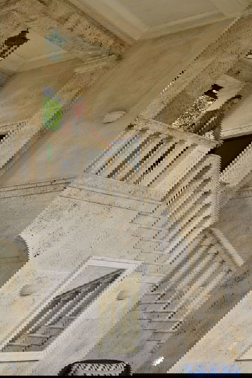 Интерьерный вид большой мраморной лестницы с балюстрадой в доме в Доминикане; мужчина стоит наверху в пространстве со штукатуркой и колоннами.