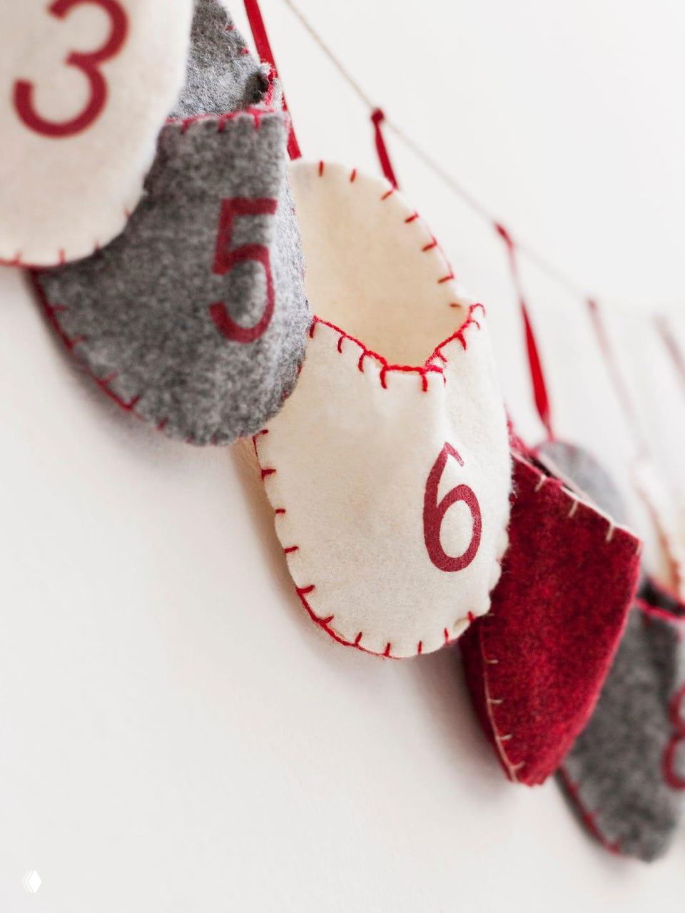 Крупный план тканевого адвент-календаря с пронумерованными мешочками на белой стене — идея для семейного праздника и украшения стены.