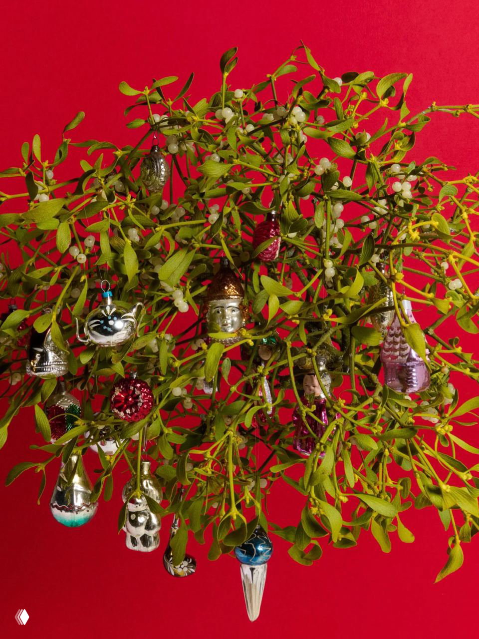 Компоновка из омелы на ярком красном фоне, усеянная множеством мелких ретро‑игрушек из серебра и цветного стекла, праздничный натюрморт.