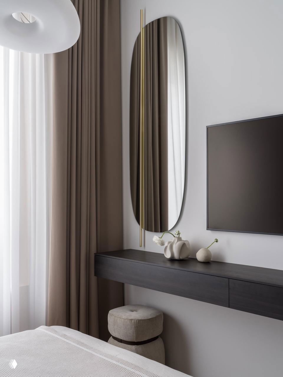 Спальня с овальным настенным зеркалом над консолью, мягкими шторами и приглушённой цветовой гаммой; акцент на простоте и функциональности мебели.