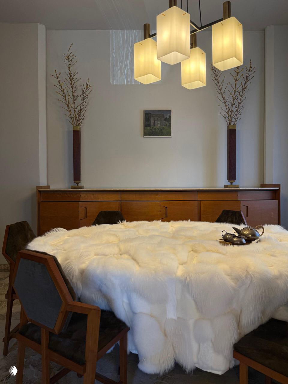 Столовая сцена на Milan Design Week: круглый стол, покрытый белым пушистым меховым покрывалом, окружён деревянными стульями и сервировкой — акцент на тактильном уюте.