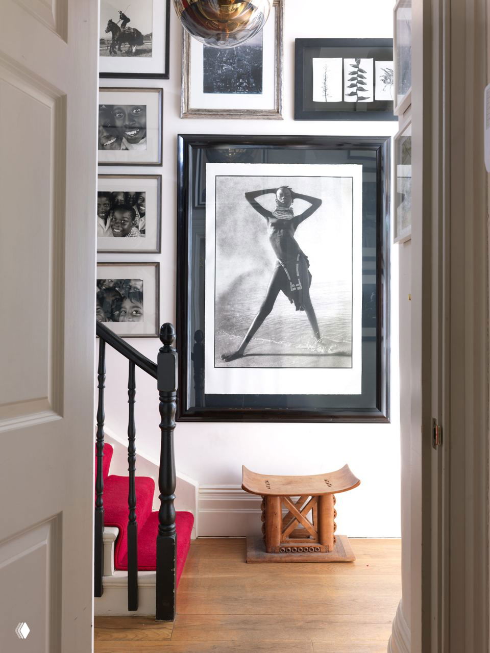 Узкая прихожая с лестницей и большим черно‑белым постером в раме, окружённым небольшой галереей фотографий — аккуратная композиция переходной зоны дома.