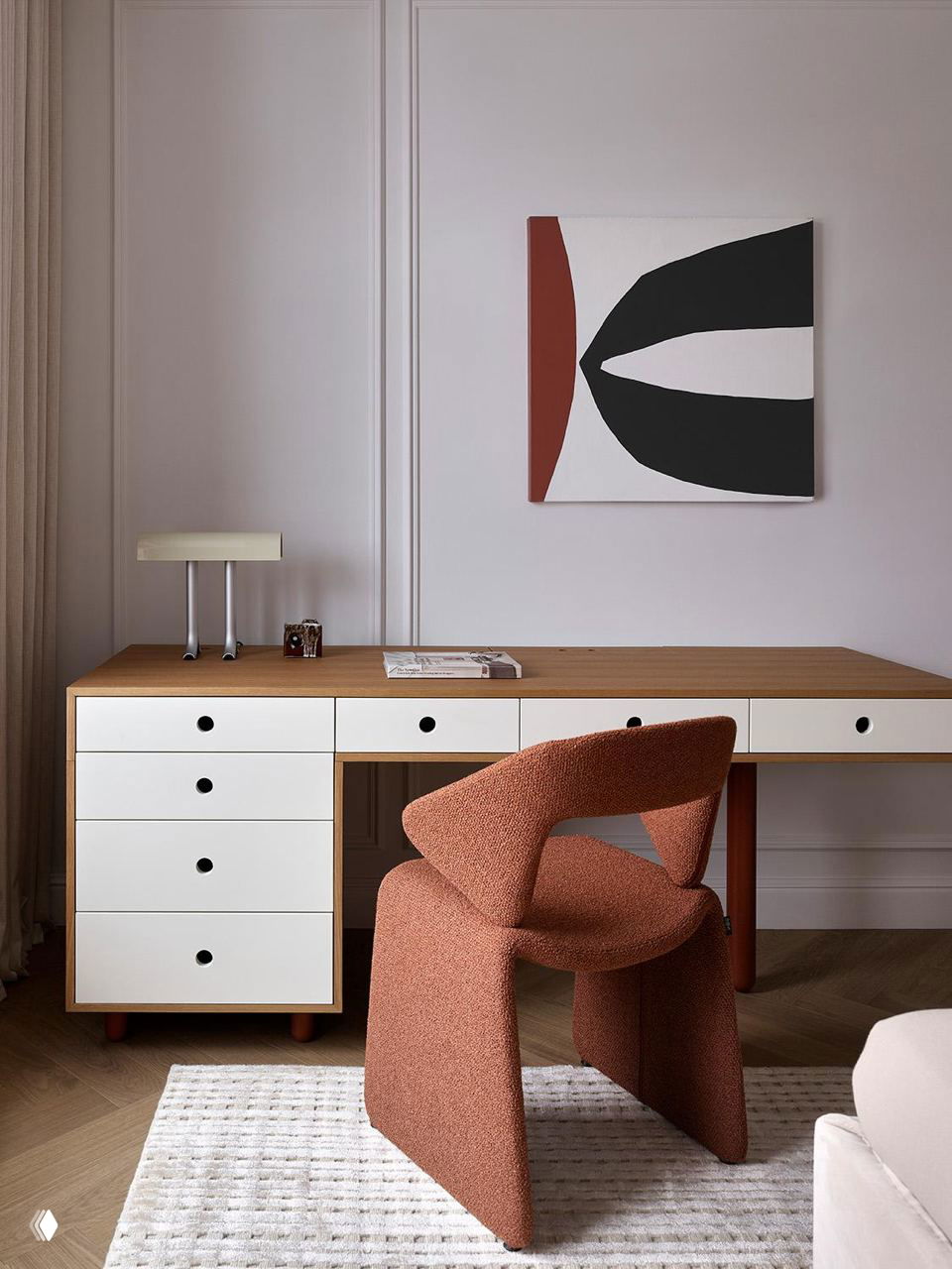 Рабочая зона с деревянным столом и ярким терракотовым стулом, минималистичная композиция и пастельная стена — акцент на форме мебели и текстуре обивки.