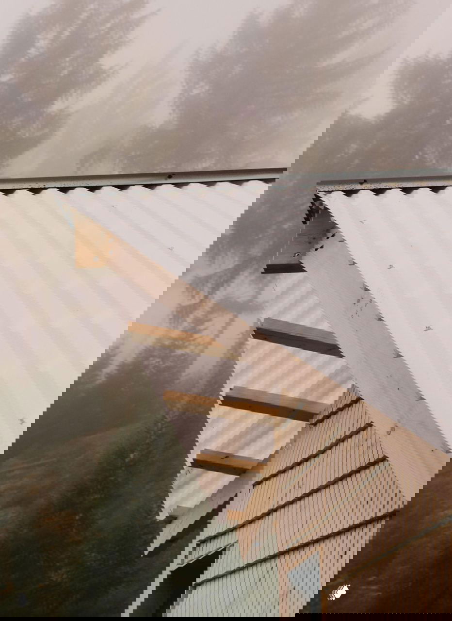 Крупный план карниза и поликарбонатной крыши сауны; видно деревянные конструкции стропил и волнистую белую крышу, устойчивую к снегу.