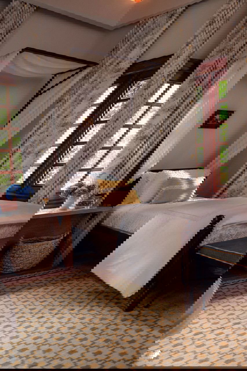 Спальня с балдахином и цветочными шторами в доме в Доминикане; деревянная мебель, мягкий текстиль и геометрический ковёр на полу.