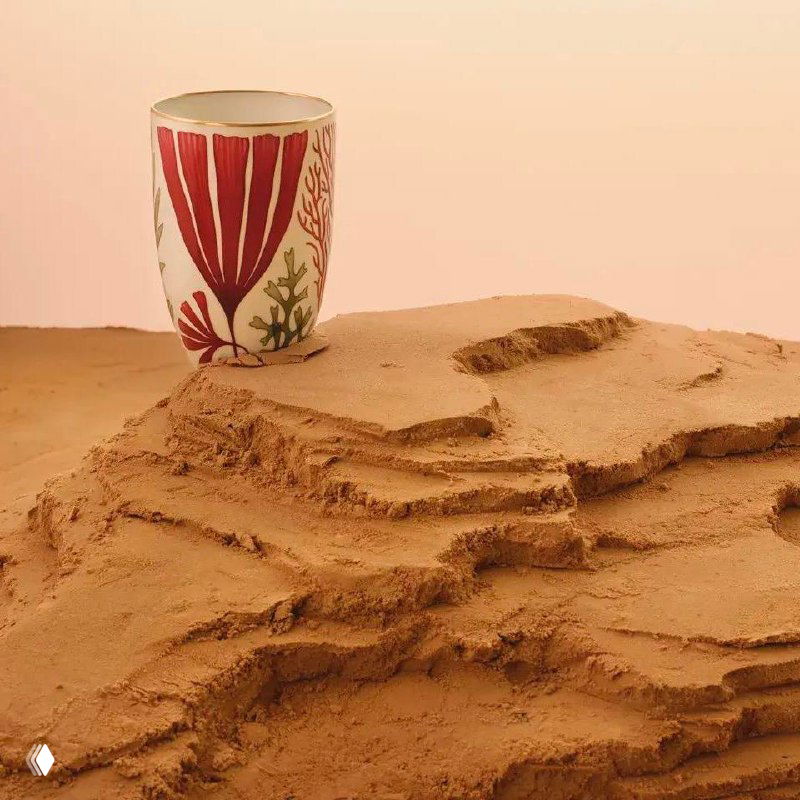 Керамический стакан Hermès с крупным красным растительным орнаментом вакаме, установленный на слоях песчаной поверхности в экспозиции