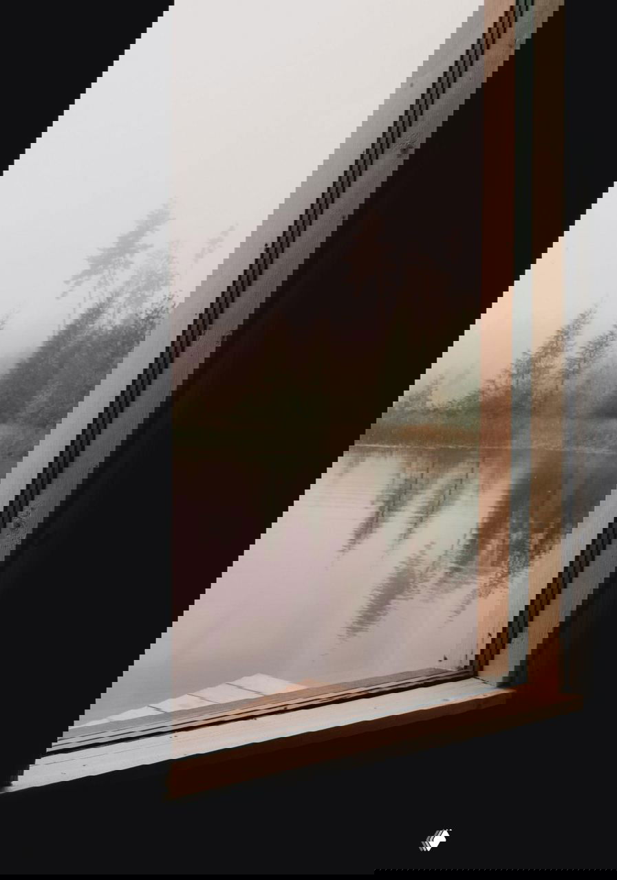 Вид из окна на озеро и лес в тумане; рама окна и деревянный подоконник очерчивают спокойный пейзаж за стеклом.