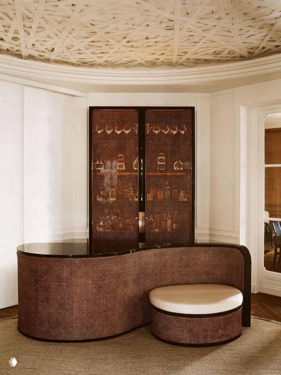 Изогнутый барный модуль с ротангом и глянцевой столешницей в классической комнате — пример тренда встроенных баров в нишах гостиной.