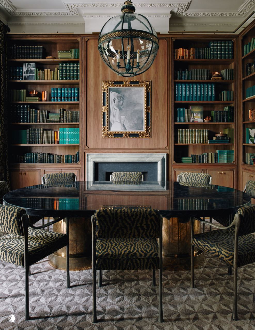Столовая, объединённая с библиотекой: деревянные книжные шкафы, чёрный круглый стол и картина в позолоченной раме над камином создают камерную атмосферу.