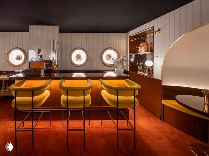 Зона сервисного обслуживания и барная часть поп‑апа: тёплая цветовая гамма, барные стулья и стойка для персонализированных услуг бренда Louis Vuitton.