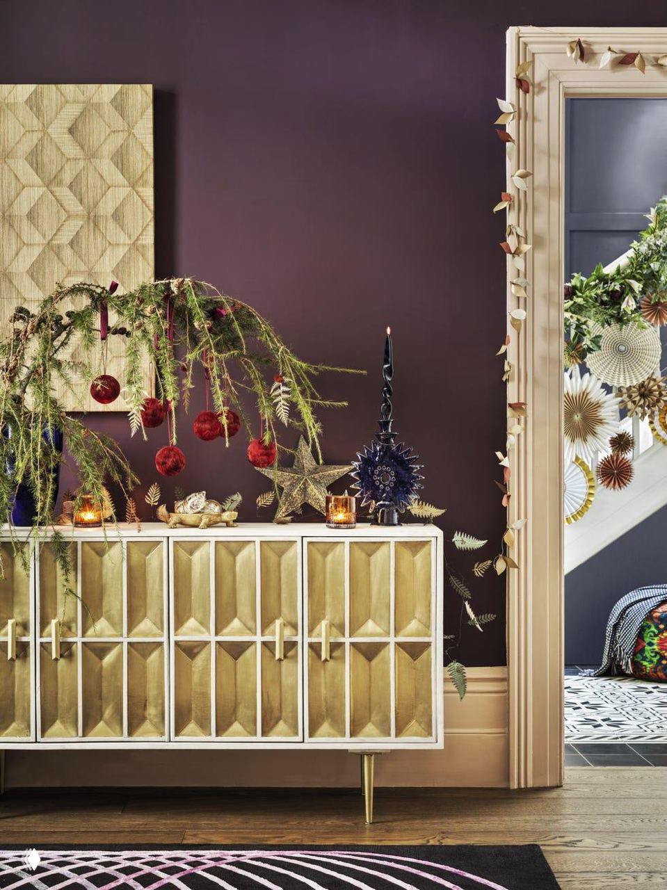 Комната с тёмными стенами, консоль украшена праздничными элементами и гирлянда на дверной коробке — насыщенные цветовые контрасты и текстуры в декоре.
