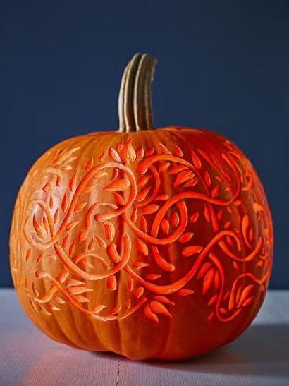 Тыква с тонкой декоративной резьбой в виде растительных узоров, крупный план демонстрирует сложную работу ножом и эффект рельефа на поверхности кожуры, акцент на мастерстве.