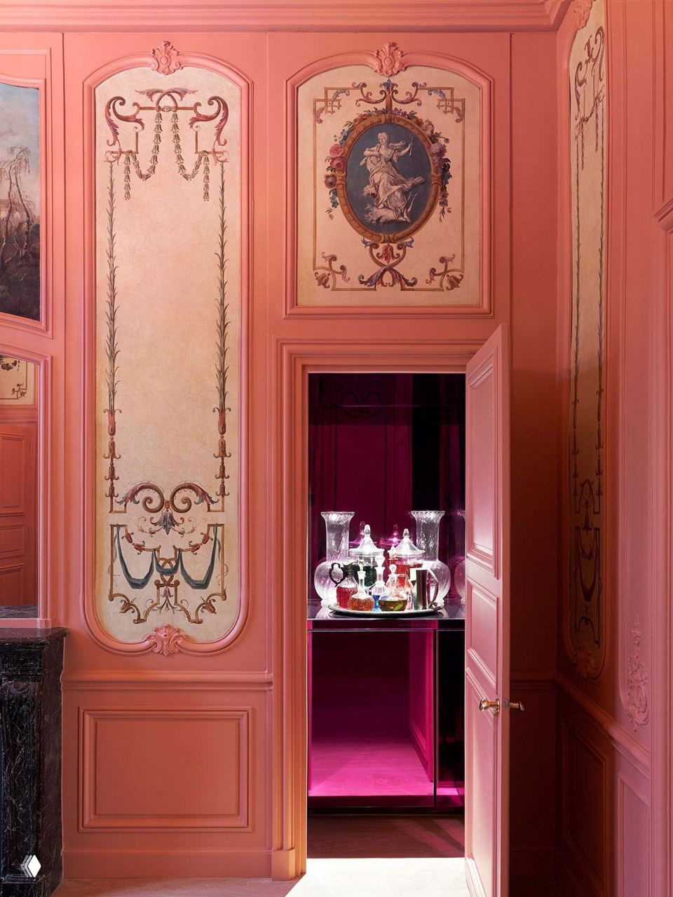 Столовая зона с яркой розовой дверью, декоративными панелями и подсветкой внутри ниши — смелые цветовые решения и театральность в интерьере.