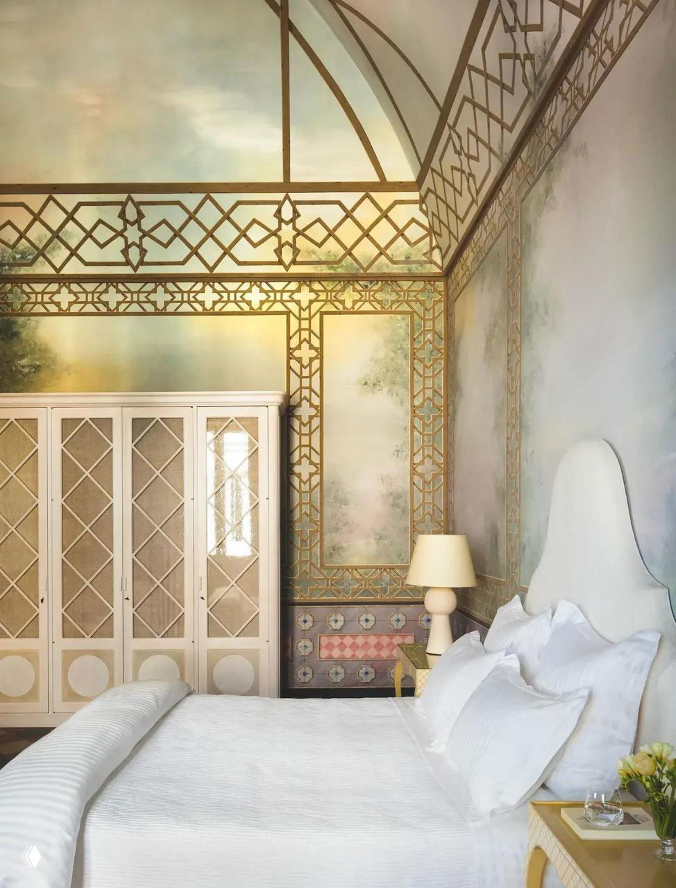 Спальня в палаццо XIX века: большая кровать с белой постелью, элегантный гардероб, настольная лампа и ажурные фрески в золотой раме, созданные для камерной атмосферы.