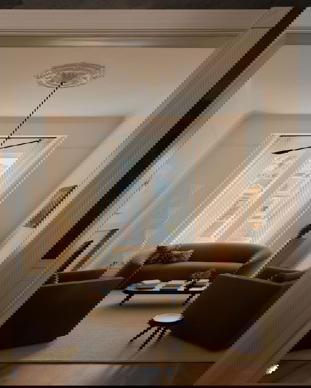 Светлая салонная зона с округлым бежевым диваном, креслами и большим окном: теплая палитра и минималистичная обстановка в классическом ключе.