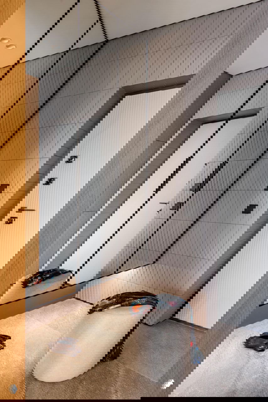 Прихожая с большим зеркалом во всю стену, серая плитка на полу, небольшой пуф и аккуратная зона для обуви и верхней одежды у входа.