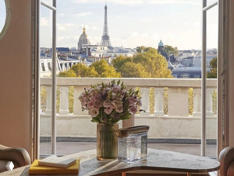 Вид из номера Mandarin Oriental Lutetia на Париж с балкона: цветы на столе на фоне Эйфелевой башни и городской панорамы.