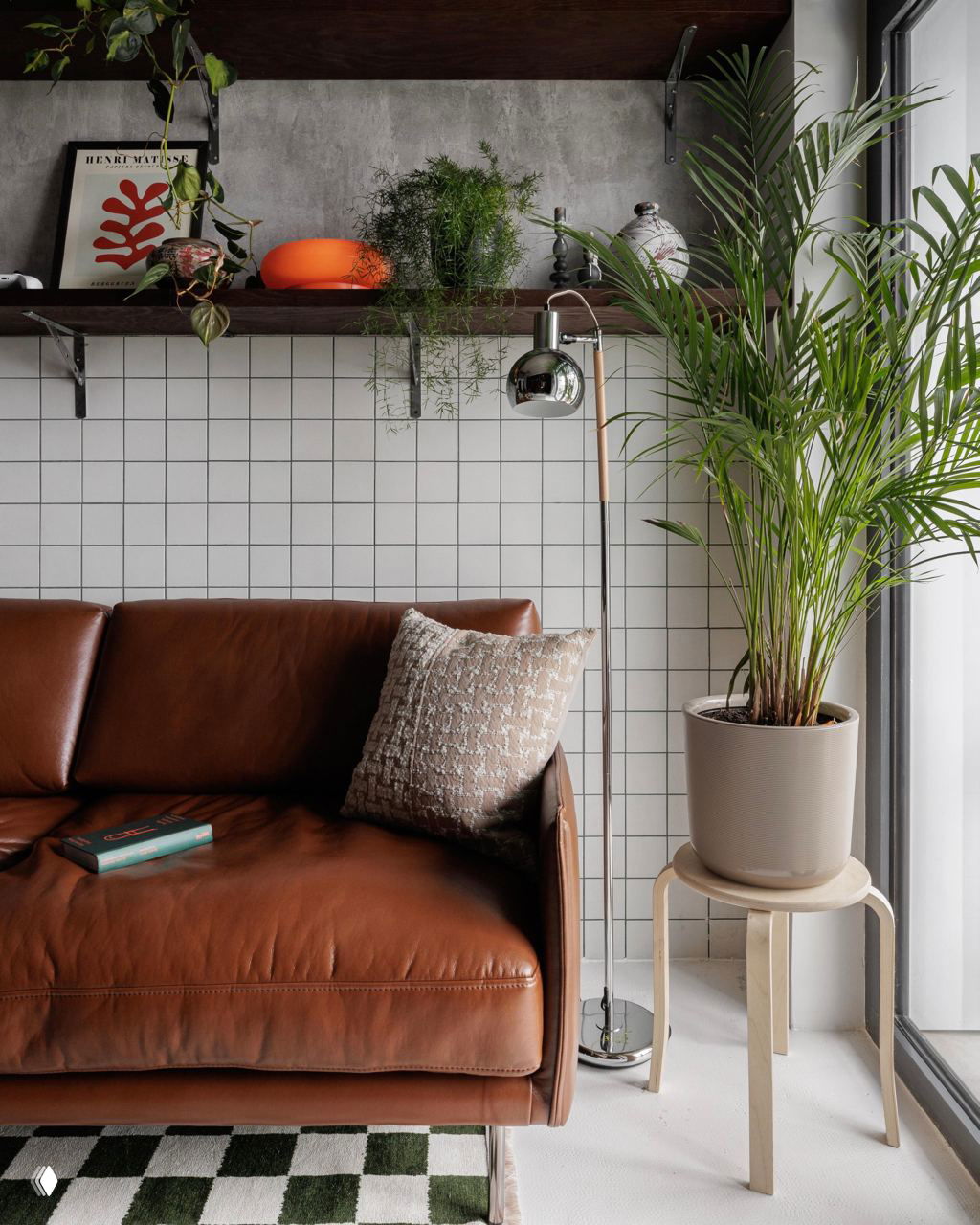 Крупный план кожаного дивана у белой плиточной стены: текстурная подушка, торшер и высокий горшок с пальмой на фоне скандинавского модерна