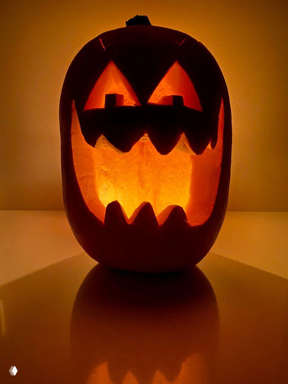 Классическая светящаяся тыква с большими треугольными глазами и широким ртом, снятая в тёплом вечернем свете на столе; подчёркнут силуэт и отражение на поверхности.