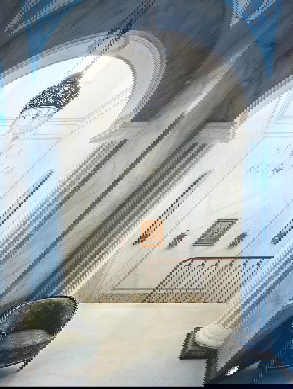 Мраморный вестибюль палаццо с высокой аркой и декоративной люстрой, колоннами и лестницей — сочетание монументальности и светлого интерьерного решения в доме-отеле.