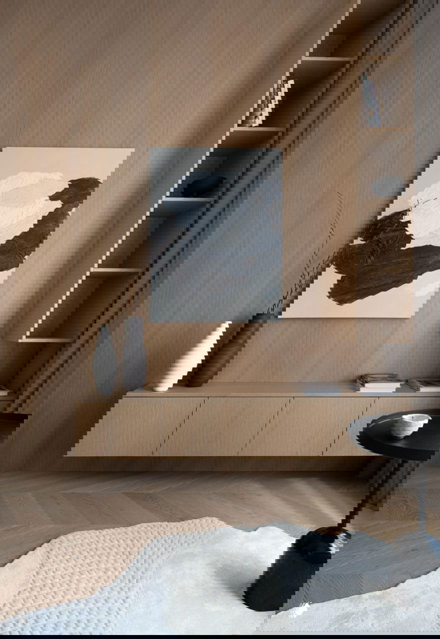 Детали интерьера: шпонированная мебель, низкая консоль, абстрактная картина и светлый фигурный ковёр на деревянном полу, акцент на текстурах.