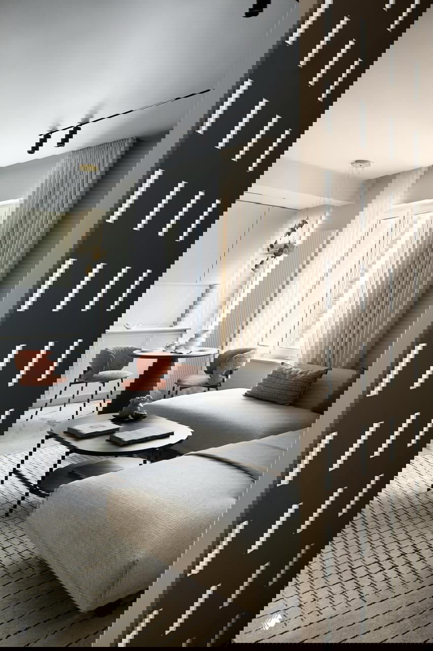 Открытая гостиная-кухня: модульный светлый диван, низкие кофейные столики и декоративная перегородка, объединяющие зоны в единое пространство.