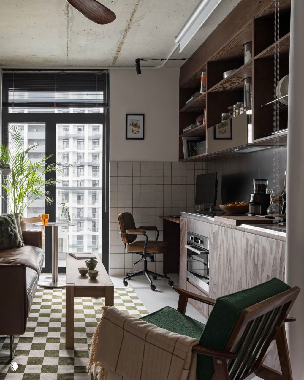 Общий вид компактной квартиры: большой оконный проём, рабочая зона у кухни, деревянные открытые полки и мебель в тёмных тонах в индустриальном стиле