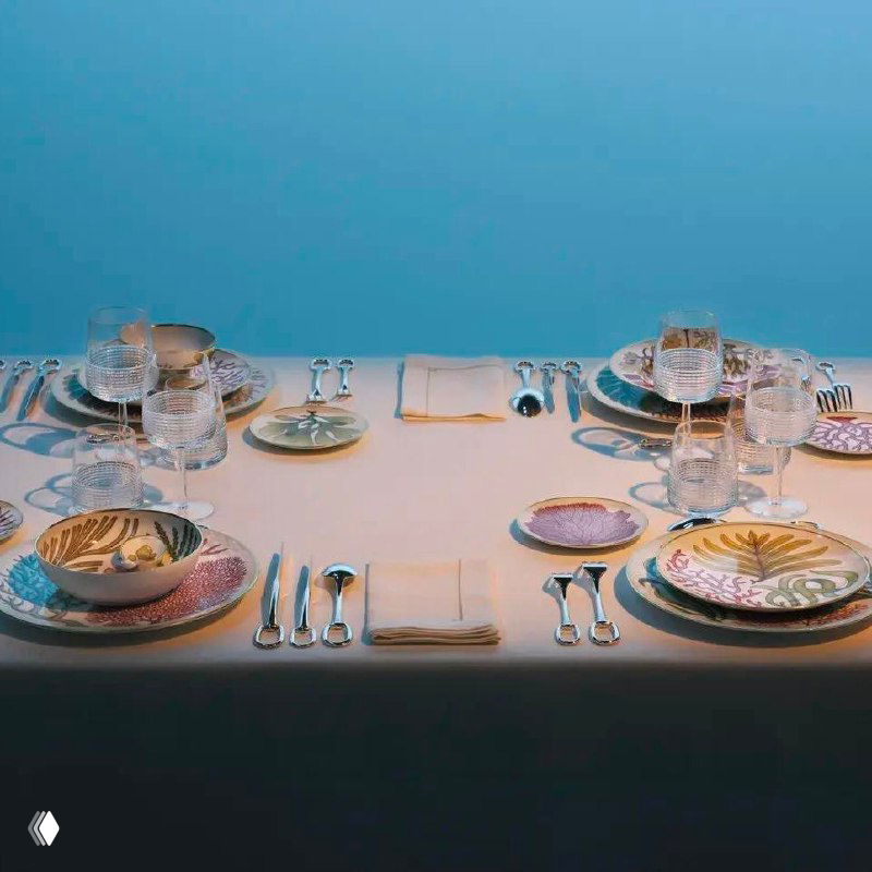 Вид экспозиции: песчаный зал с локальными световыми пятнами, на которых выставлены одиночные тарелки и чаши коллекции Natures Marines от Hermès