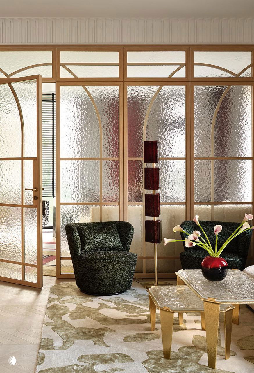 Интерьерная сцена с высокими окнами: кресло в авторской обивке, плотные шторы, ламели на окне и игра света на деревянном полу и декоративных поверхностях.