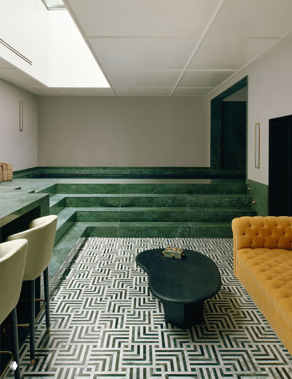 Помещение с зелёными мраморными ступенями и чёрно-белой плиткой, низкая диванная группа и журнальный стол — акцент на материале и графическом узоре пола.