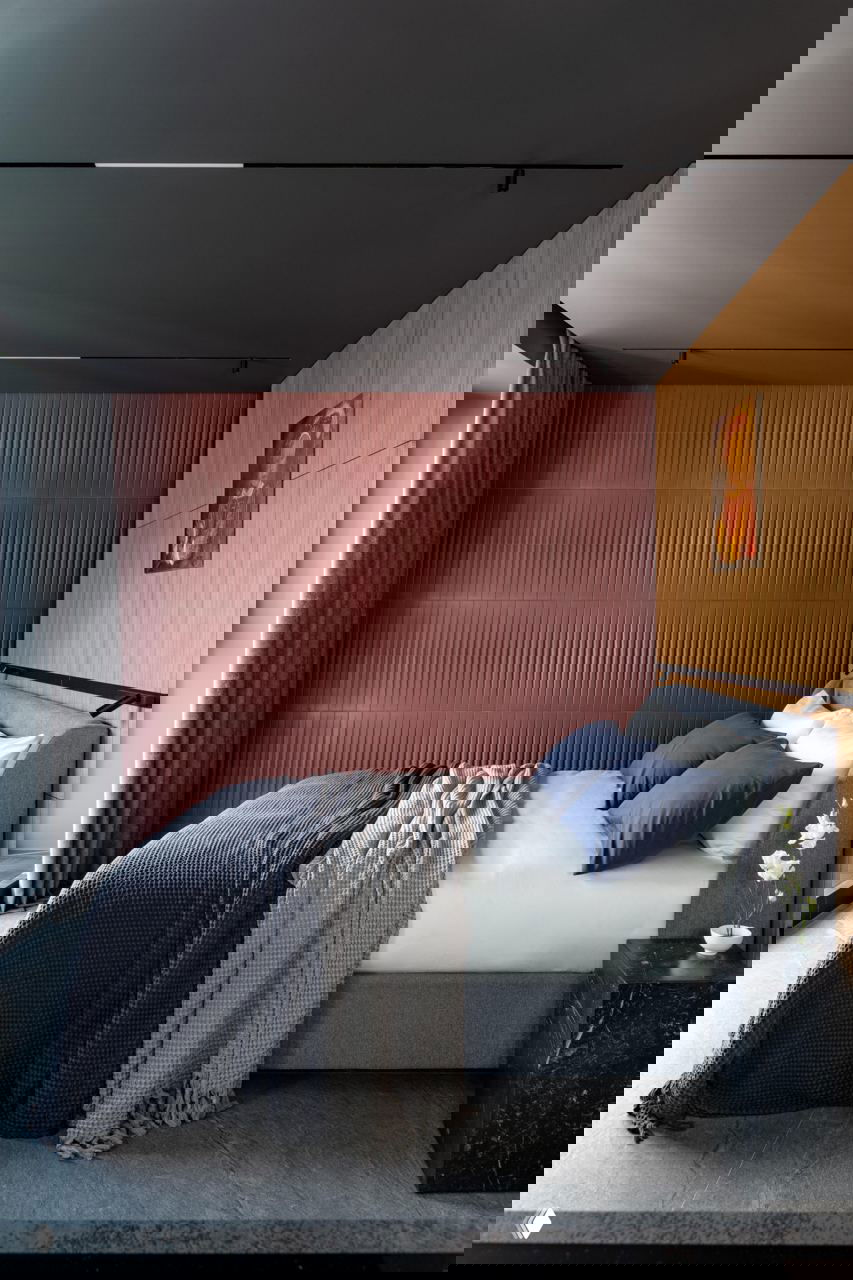 Полный вид спальни с серой кроватью, темным потолком, бордовой фактурной стеной и декоративными пледами и подушками, создающими уютную атмосферу.