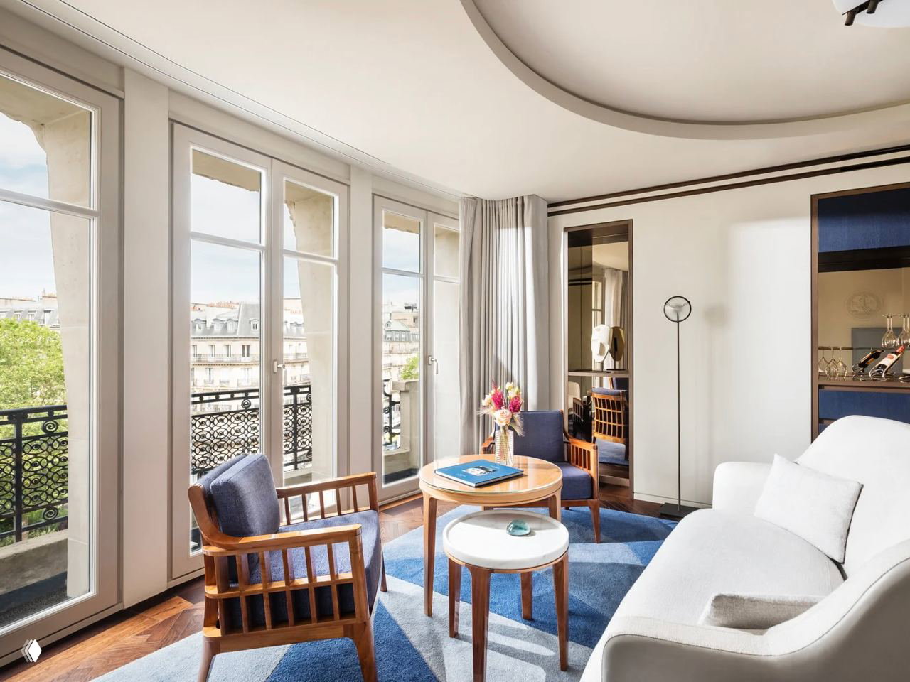 Гостиная зона номера Mandarin Oriental Lutetia: деревянная мебель, синие акценты в текстиле и большая панорамная дверь на балкон с видом на Париж.