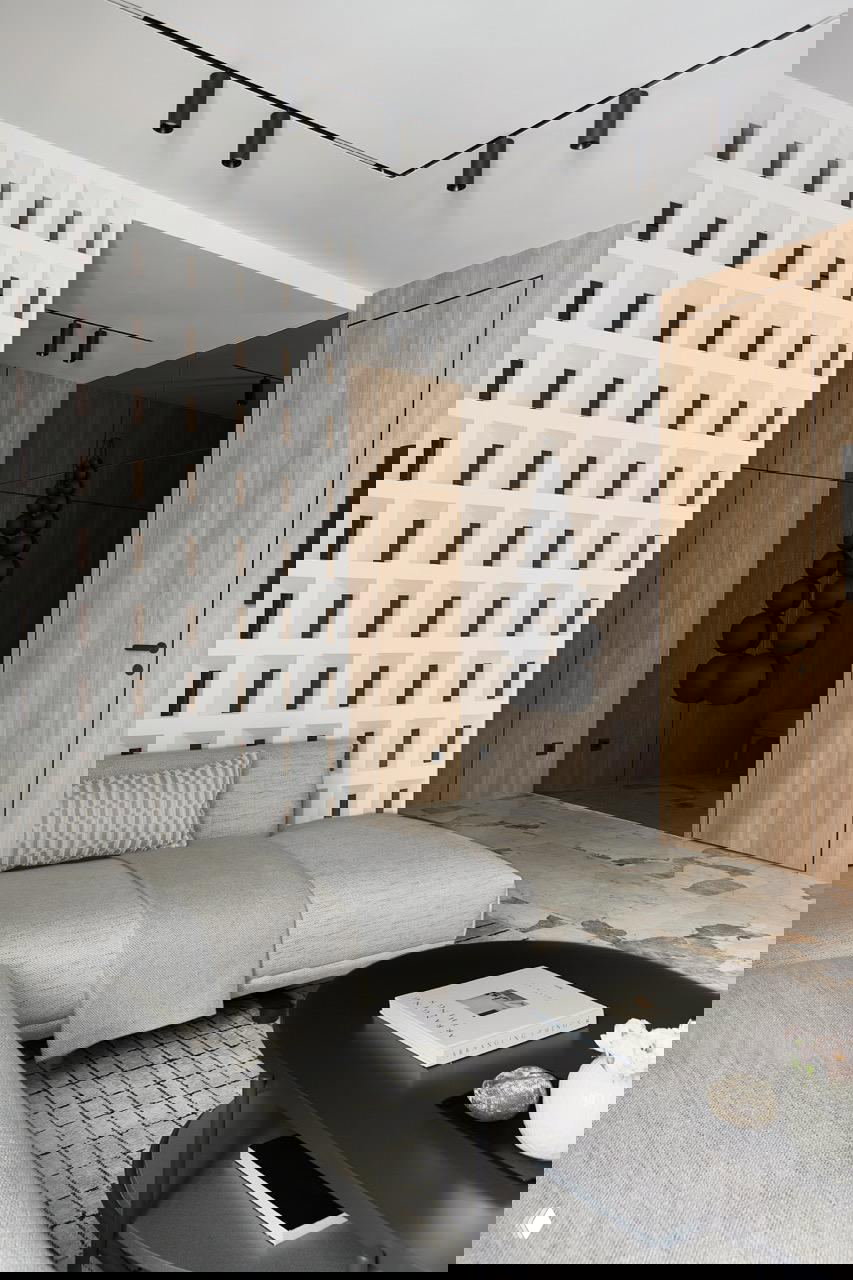 Гостиная с белой перфорированной перегородкой, светлым диваном на фоне деревянной стеновой облицовки и контрастных декоративных элементов у прохода.