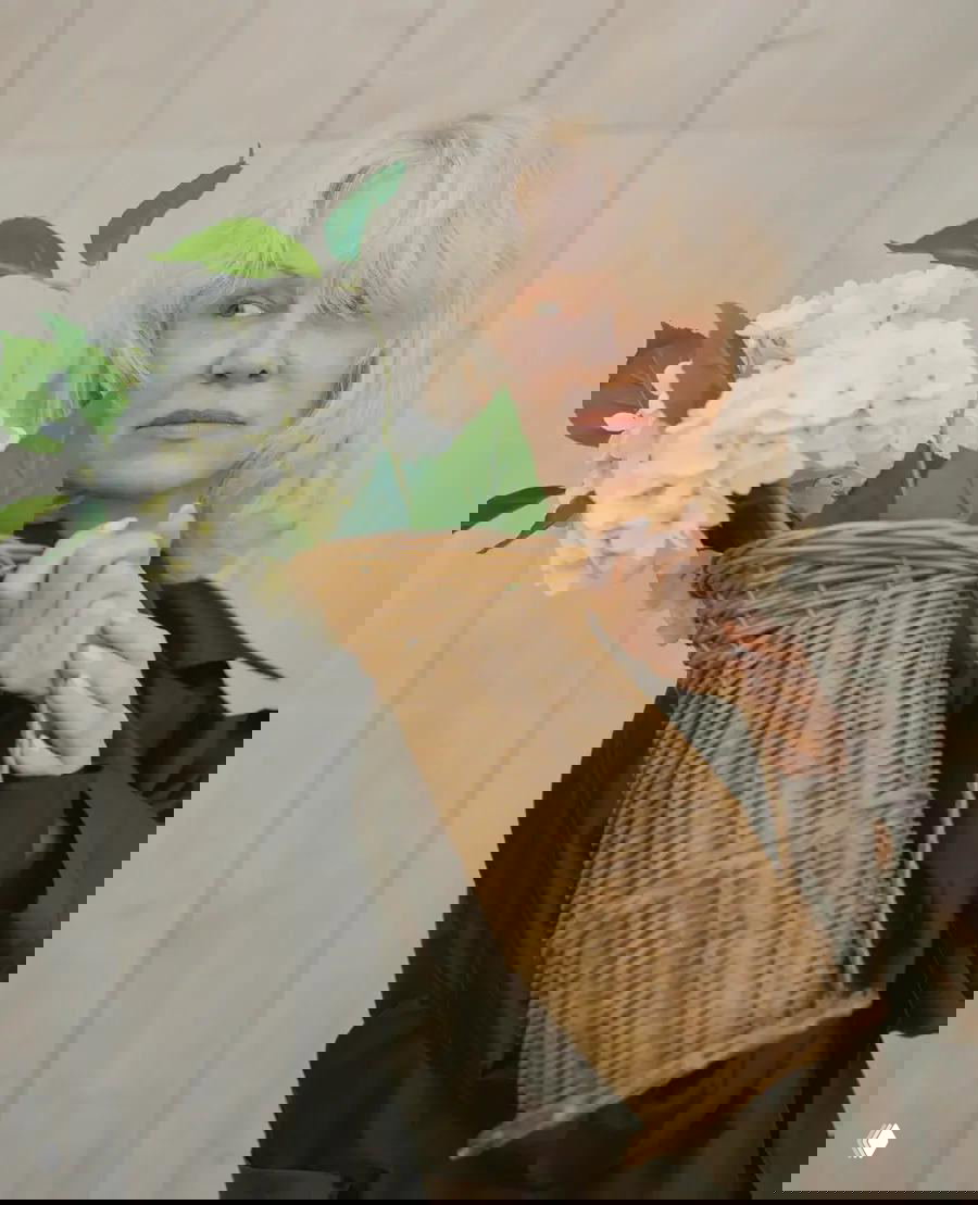 Крупный план женщины, держащей плетёную корзину с белыми гортензиями; мягкий естественный свет подчёркивает текстуру ротанга и цветы.