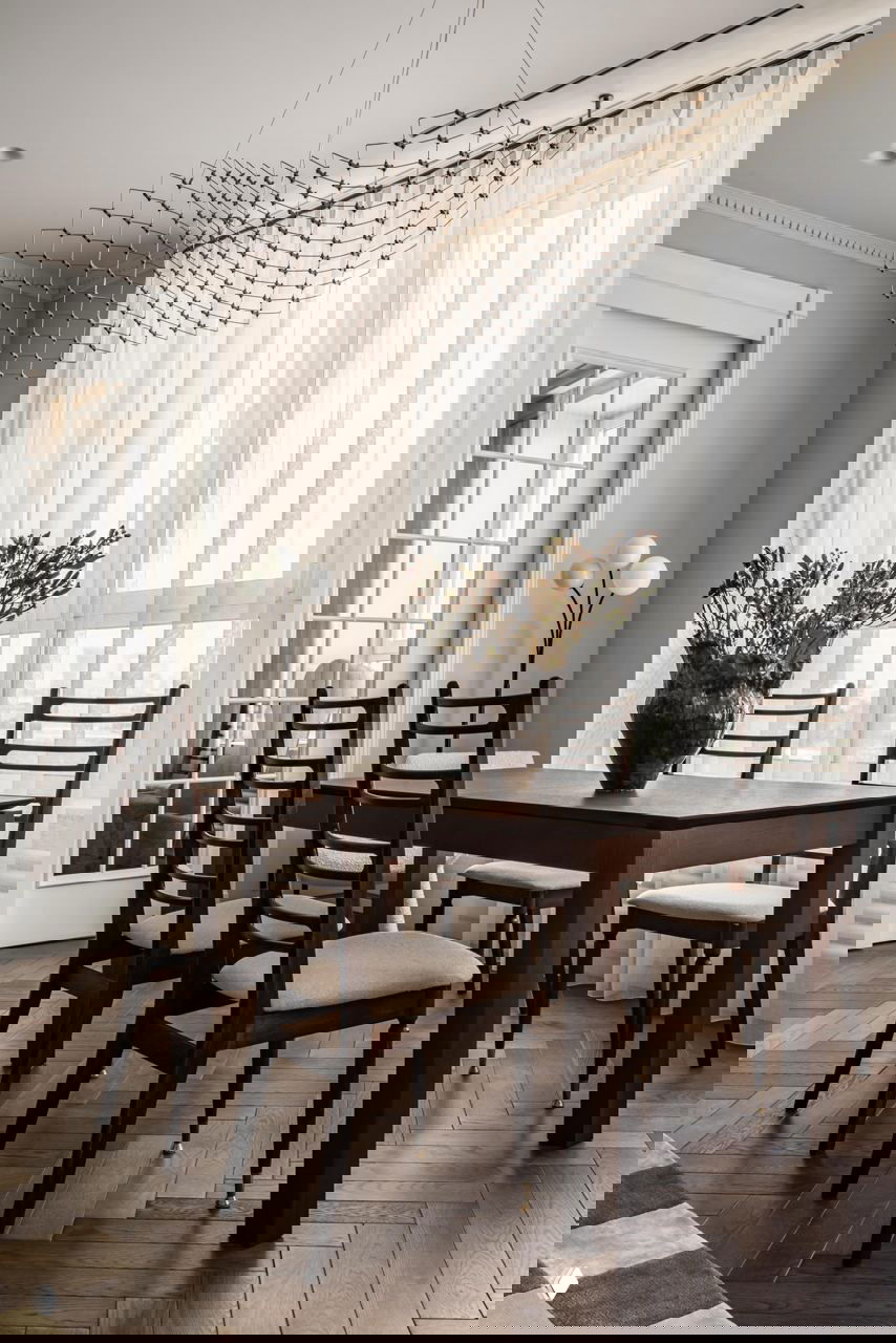 Столовая зона с тёмным деревянным столом, стульями в классическом стиле, большой вазой с сухоцветами и воздушной ажурной люстрой над столом.