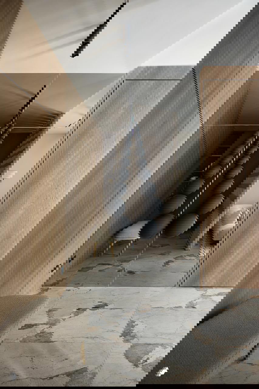 Прихожая с зеркальным шкафом и скульптурной инсталляцией из чёрных шаров на подвесах, тёплая деревянная отделка стен и мраморный пол одного рисунка с общим интерьером.