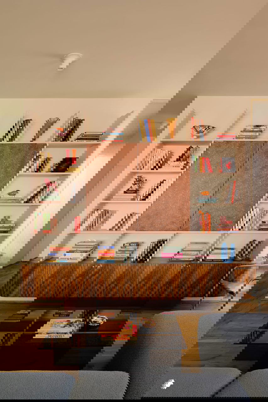 Гостиная с большой стеллажной системой, книгами и низкой мебелью из темного дерева на фоне деревянного паркета и мягкого освещения.