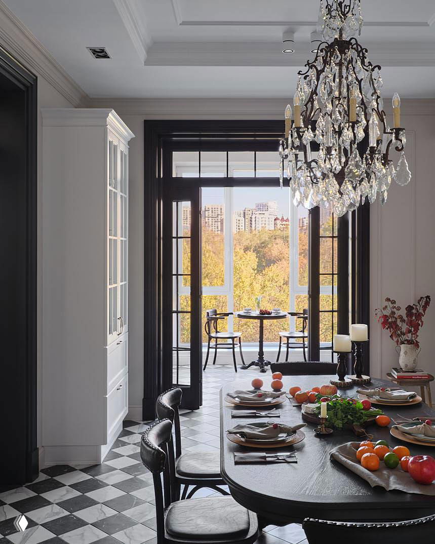 Вид из столовой на большие панорамные окна и балкон: сервированный тёмный стол, свечи и светлый городской пейзаж за стеклом в фоне под люстрой.