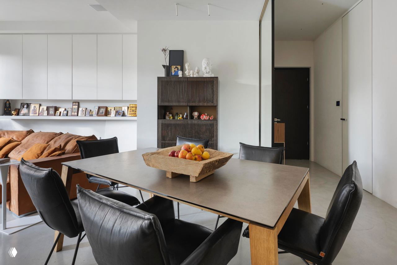 Обеденная зона и стеллажи: деревянный стол, чёрные кожаные стулья и открытые полки с семейными фотографиями и декором на фоне светлой стены.