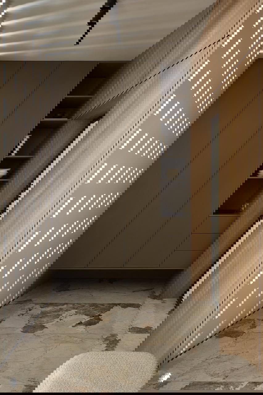 Узкий входной коридор с перфорацией, высокими тёмными встроенными шкафами, скамьёй и крупными мраморными плитами на полу, сохраняющими единую палитру проекта.