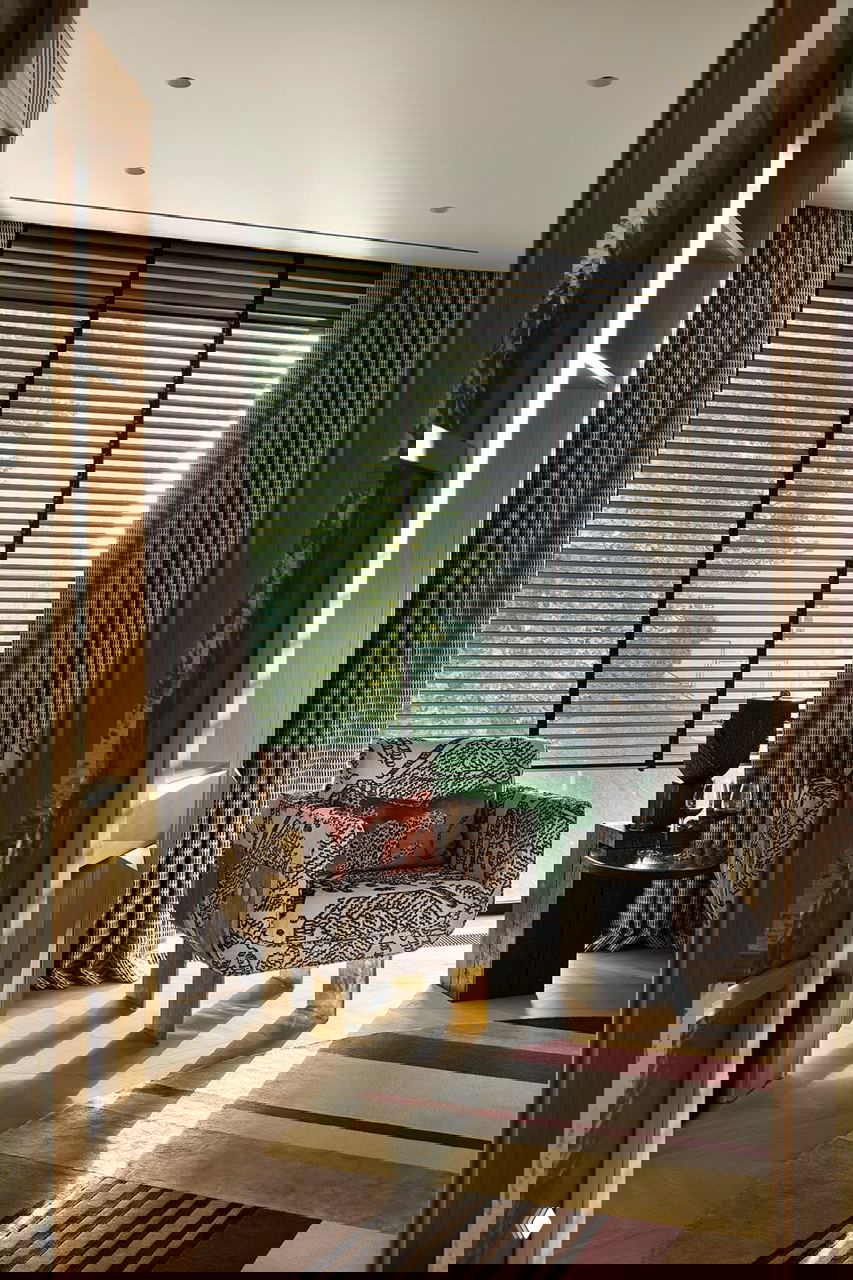 Комфортабельный уголок с креслом и небольшим столиком у большого окна: дневной свет, плотные шторы и декоративная роспись на текстиле создают уютную читальную нишу.