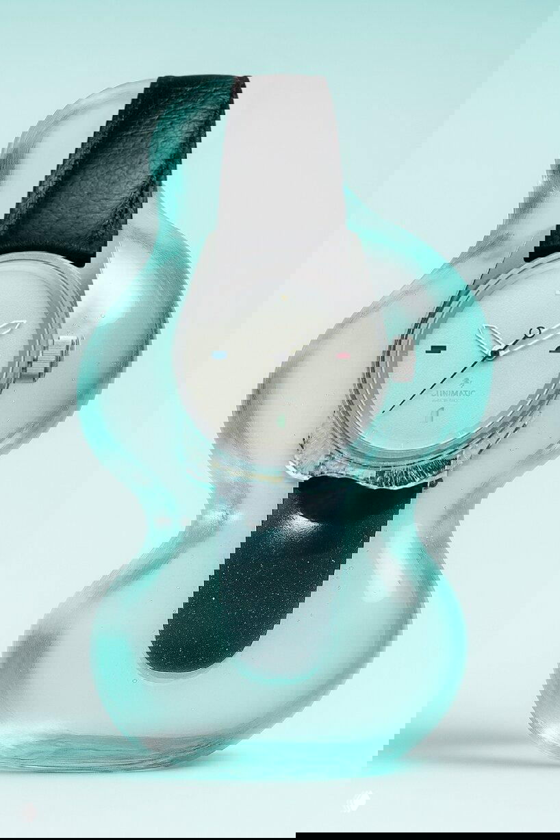 Часы Unimatic Modello Cinque U5S-NS на бирюзовом фоне внутри прозрачной жидкой стекловидной формы; виден кожаный ремешок и цветные проёмы на циферблате.