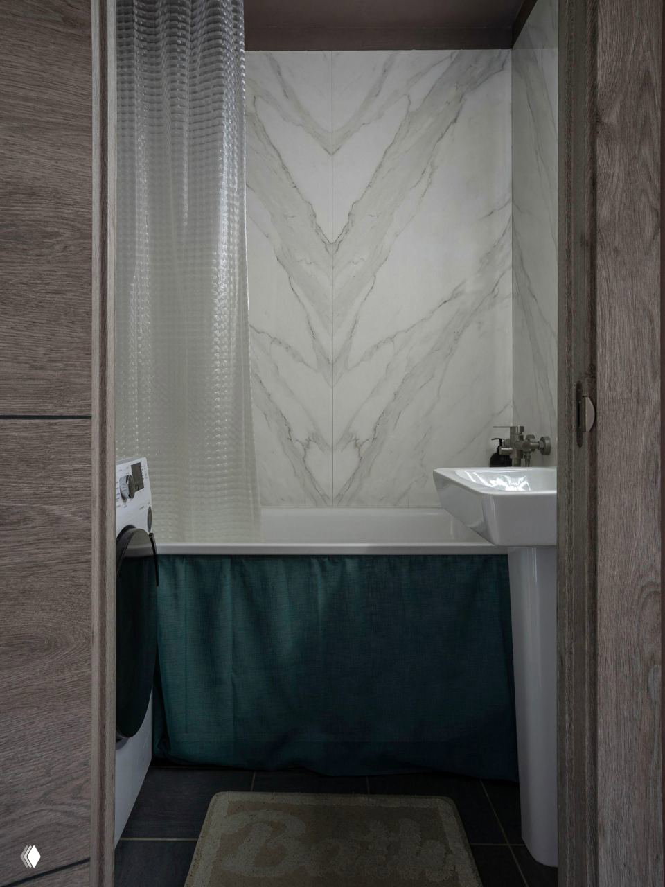 Ванная комната с мраморным панно на стене в зоне ванны, прозрачной занавеской и тёмной плиткой на полу — контрастные текстуры и сдержанная палитра
