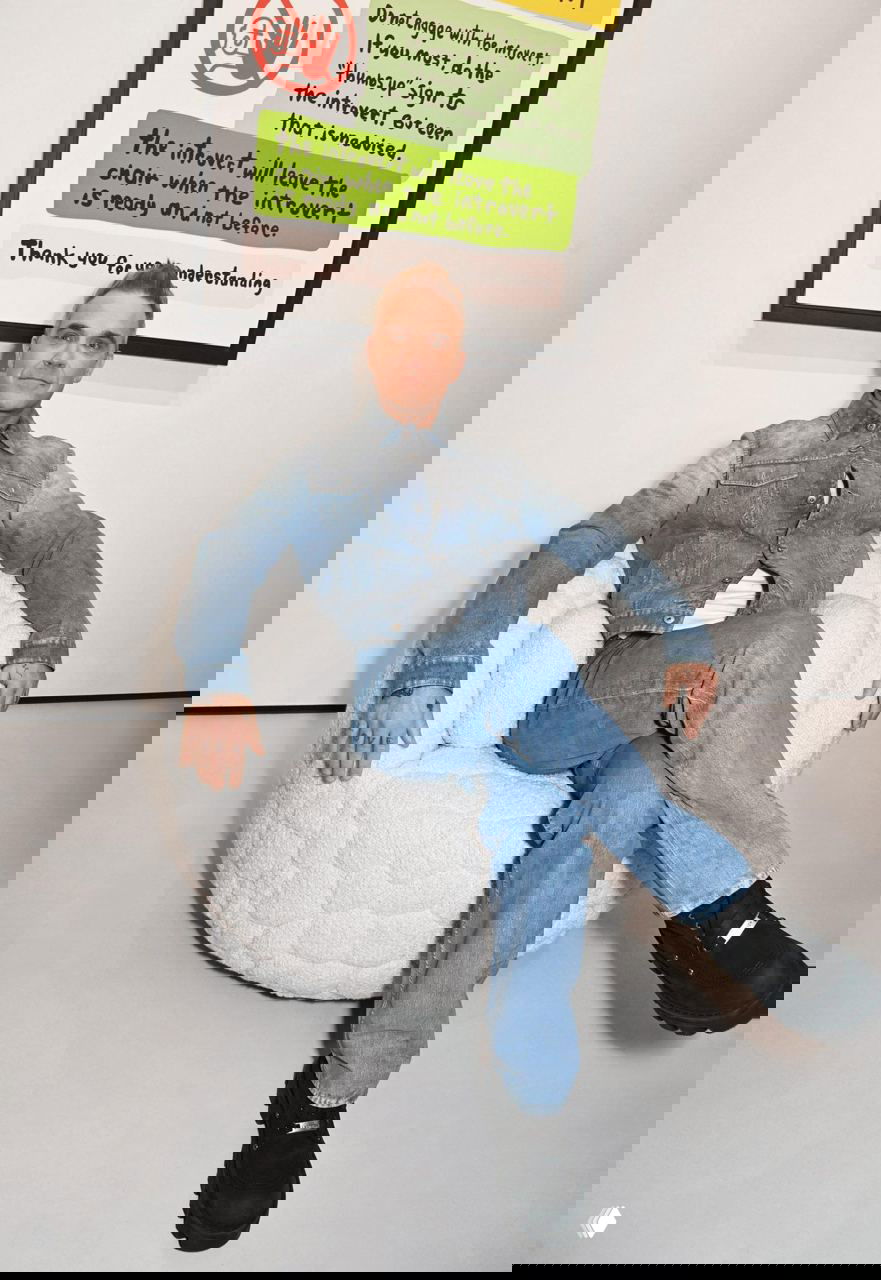 Человек в джинсовой куртке сидит в округлом кресле Introvert в выставочном пространстве; кресло подчёркивает масштаб и форму.